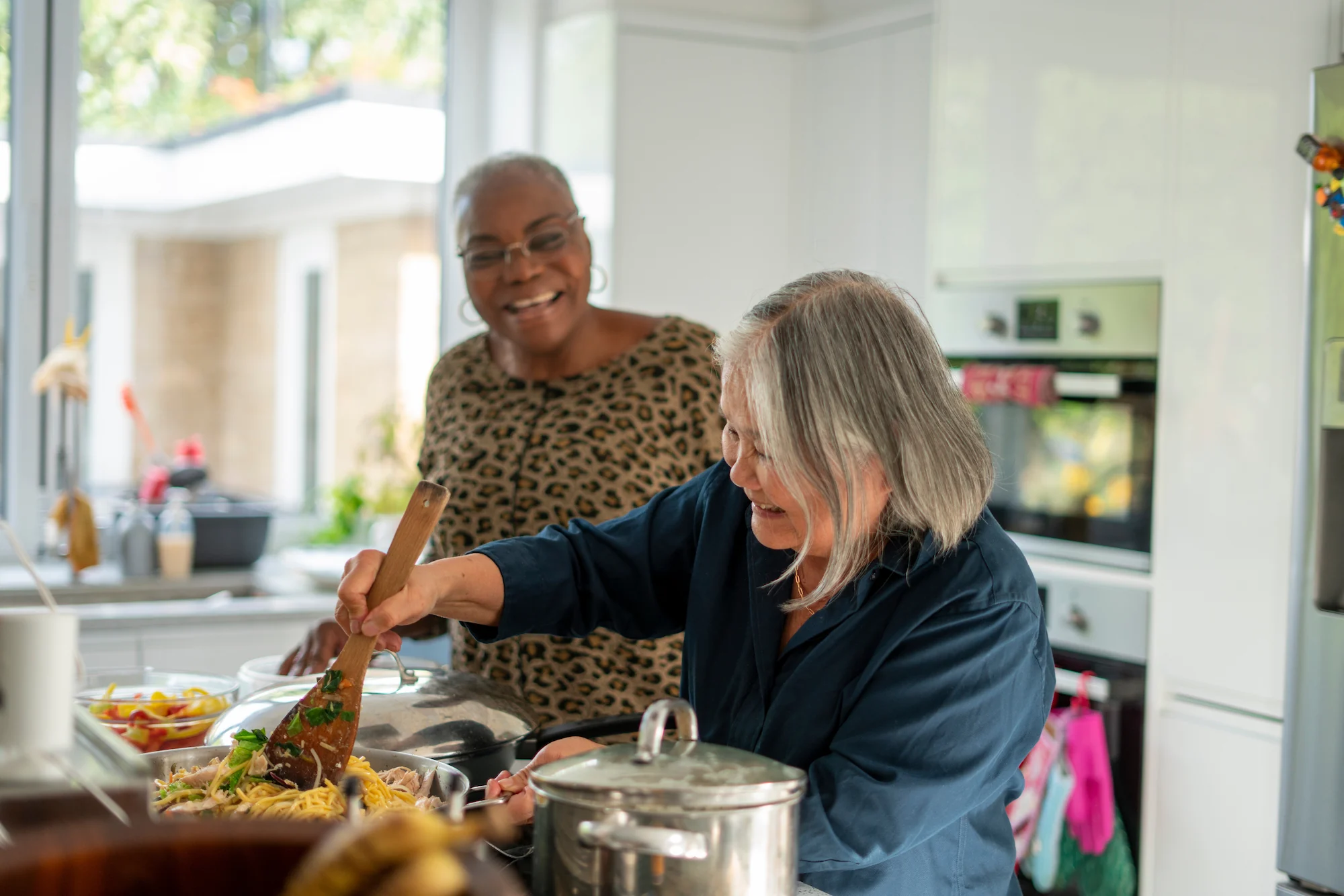 Two women cooking together in a kitchen, one stirring a pot of food